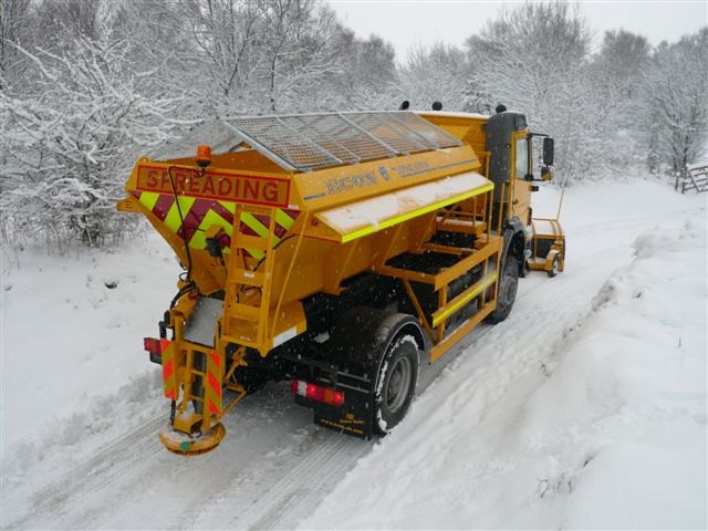 雪の積もった道を進む英国の散布車